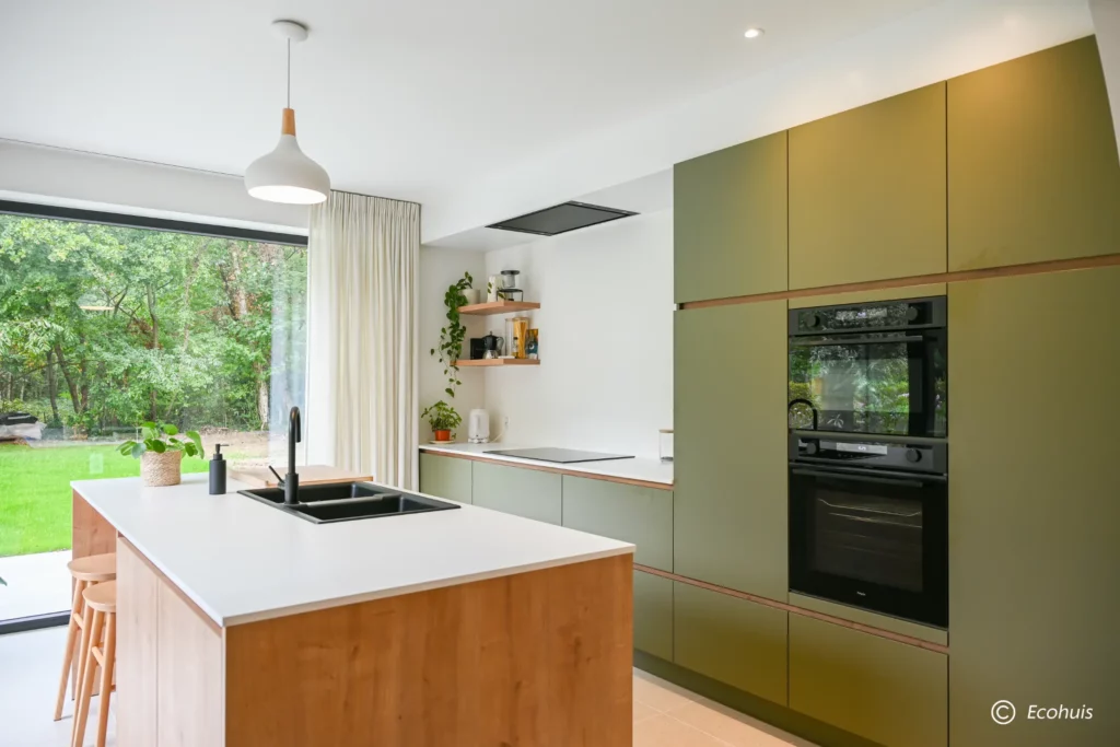 Groene keuken met eiken eiland en wit werkblad, groene kastenwand met ingebouwde ovens
